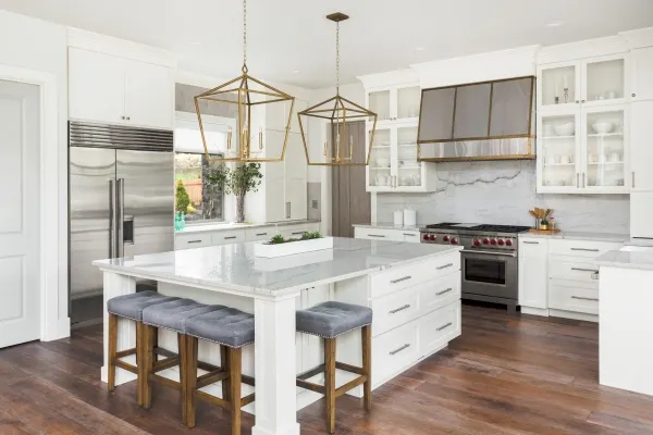 Beautiful white kitchen in luxury home. Features large island, pendant lights, and hardwood floors