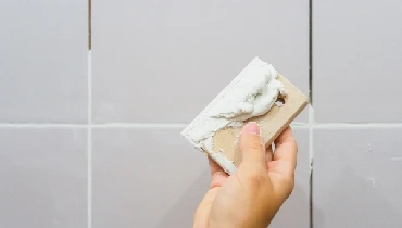 Female holding grout on a spreader with bathroom tile in the background.