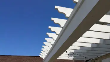 The top of a white pergola against a clear blue sky.