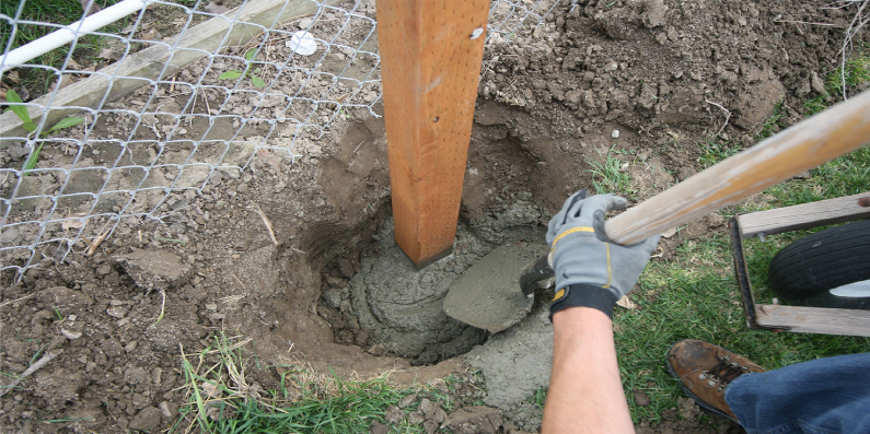 shovel putting cement on fence post