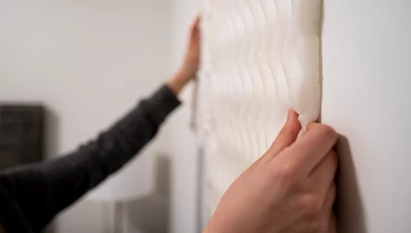 Person holding a white soundproof foam panel against a wall.