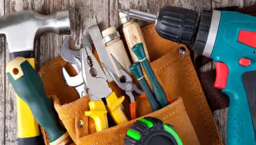 Tools used for various jobs that could be completed by a professional handyman, including a drill, hammer, and various hand tools in a toolbelt.