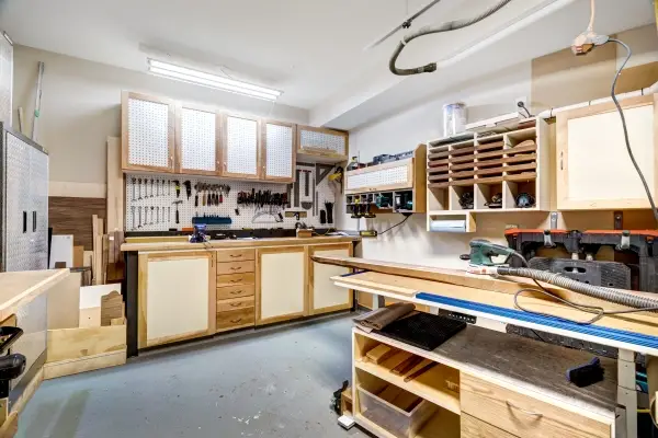 Garage workshop for cabinet making and wood working with tools and equipment organized neatly on wall and in cabinets.