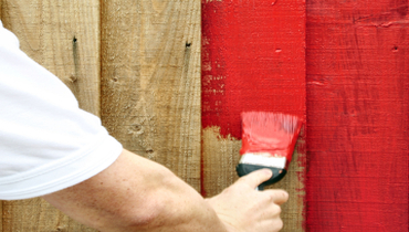 Someone painting a wooden fence red.