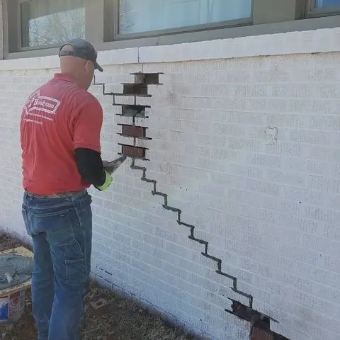 A handyman replacing bricks and reapplying mortar to a white stone wall during an appointment for masonry repair in Wichita, KS.