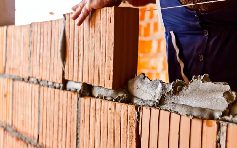 A stone mason in the process of applying mortar and laying bricks during a masonry project.