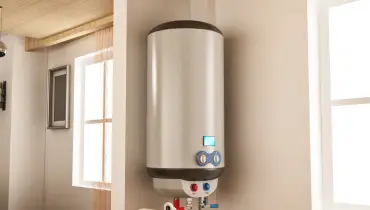A modern hot water heater hanging in the corner of a room where it has just been installed.