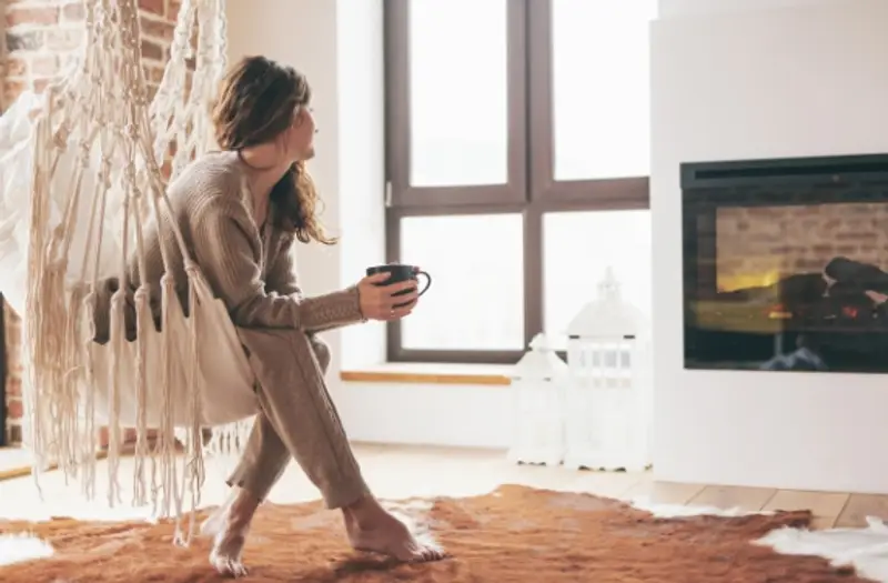 Young woman holding a coffee cup relaxing in front of an electric fireplace