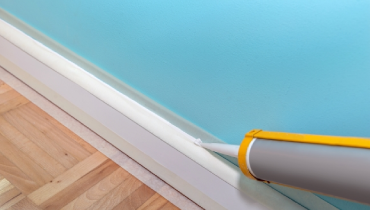 A person using a caulking gun to apply caulk to a baseboard