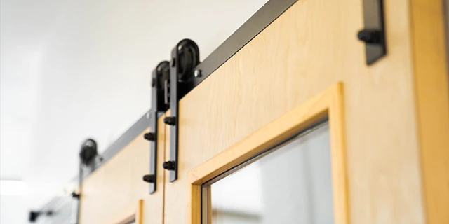 The top of an installed sliding barn door, with pale-yellow-stained wood doors and black-powder-coated steel hardware.