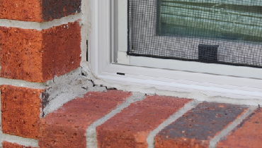 Dried worn-out caulking around exterior windowpane of brick home