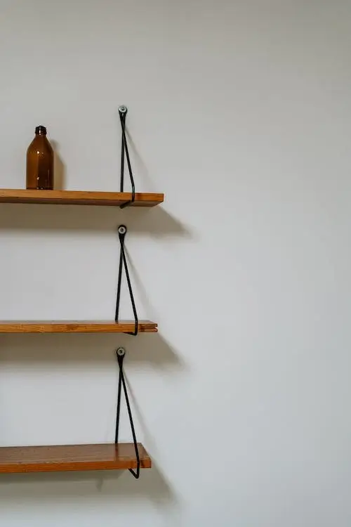Three wooden shelves against a white wall. The shelves are held up by black metal pieces on the end.