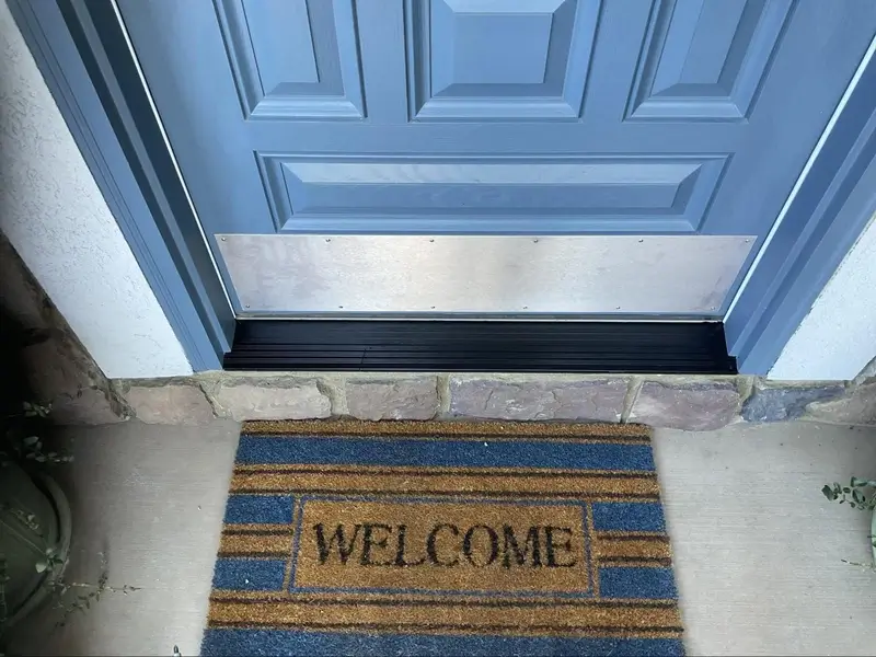 An image of a blue door with a metal bottom. On the ground in front of it is a welcome mat with blue stripes.