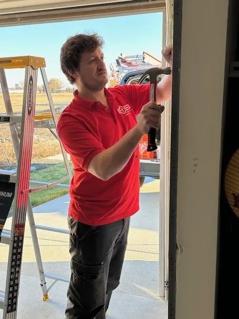 A Mr.Handyman service professional uses a hammer on a wall.