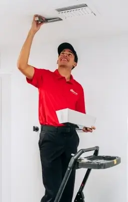 A smiling Mr.Handyman professional service professional is standing on a ladder, inspecting the ceiling.