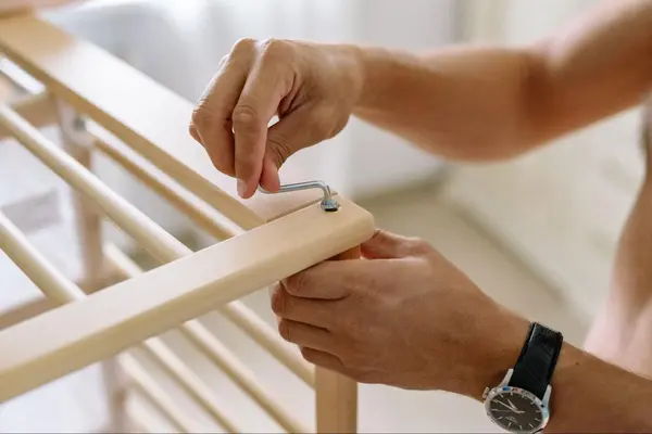 Two hands are in frame. One hand is holding a wooden furniture frame and the other is using a wrench to tighten in a bolt.