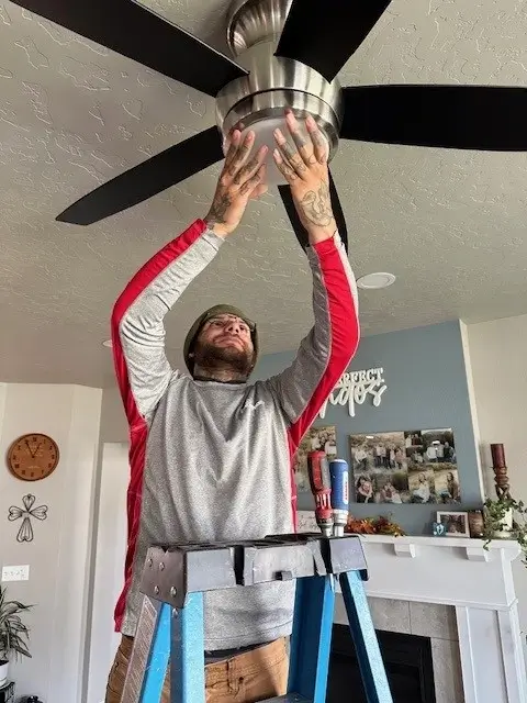 a man in a grey and red sweater is installing the light into a ceiling fan.