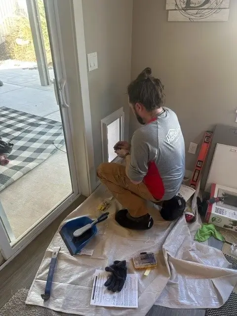 A Mr.Handyman service professional installs a pet door in a wall next to a sliding glass door.