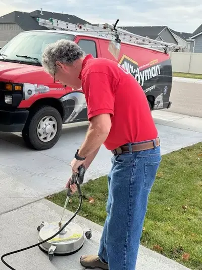 A Mr. Handyman service professional uses a surface pressure washer to clean a front driveway.