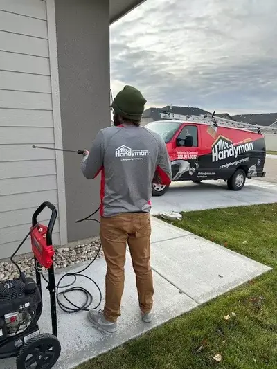 A Mr. Handyman service professional stands next to a house holding a pressure washer.
