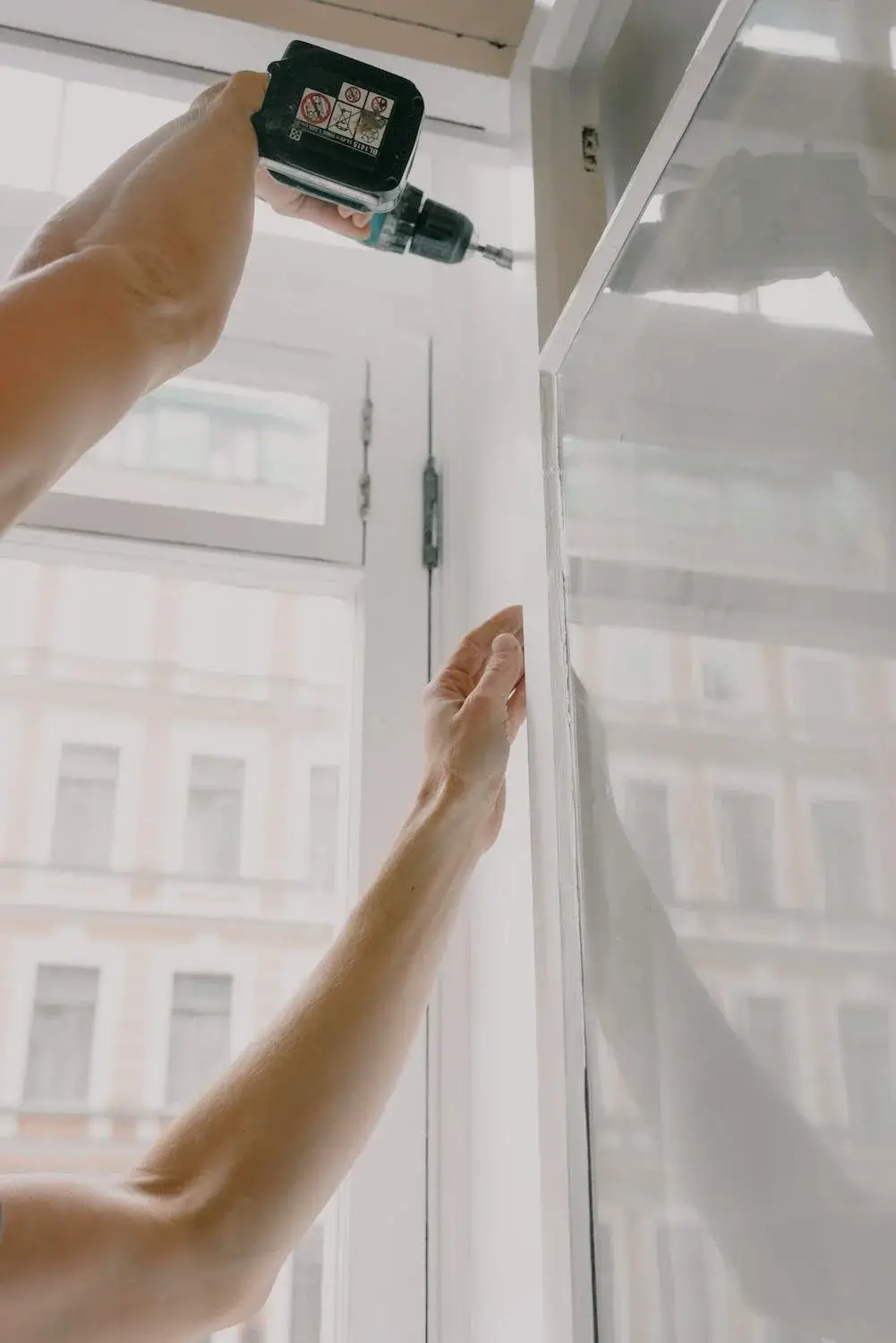 Two arms reach forward holding a drill to install a large window.