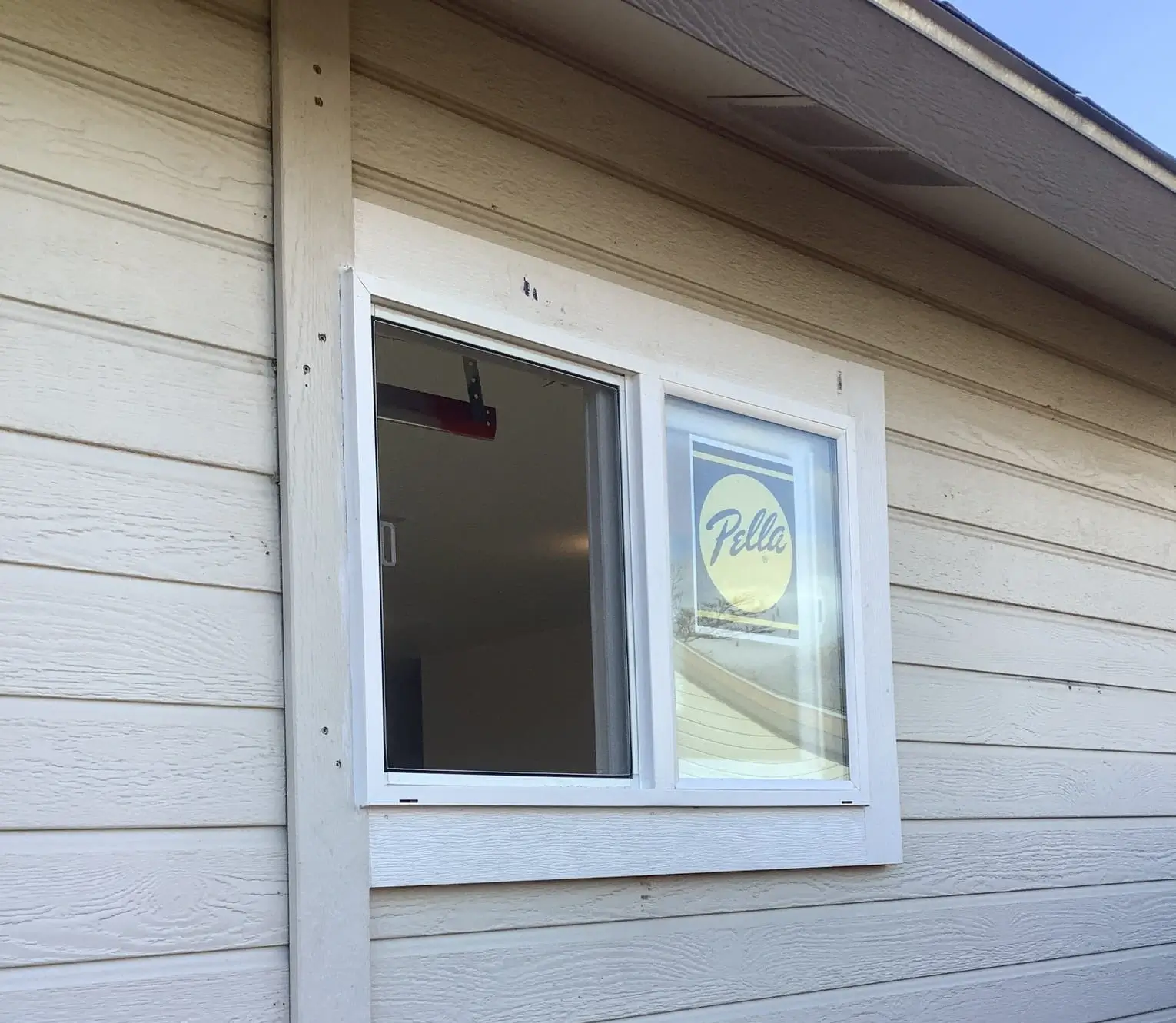 A newly installed window on the side of a house. The window has a Pella brand sticker on it.