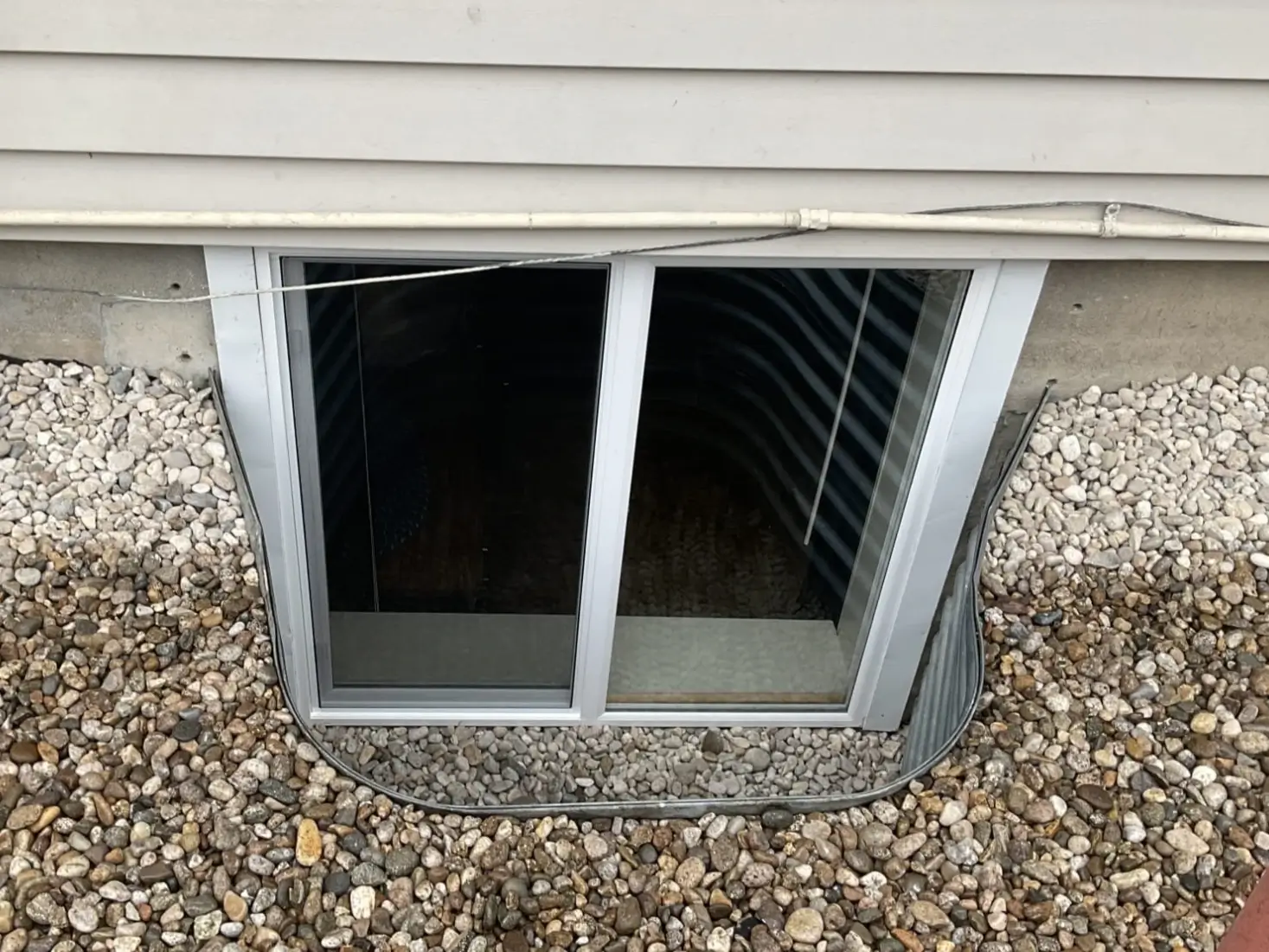 A client testimonial image of a white trimmed window in a partial basement. The ground around it is covered in gravel.