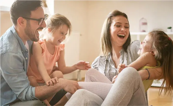 Couple and two young girls smiling and laughing in warmly lit room.