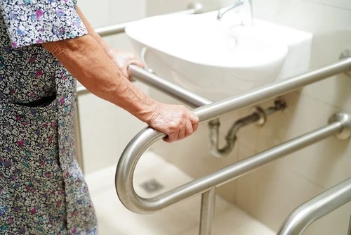 Senior woman holding on to hand rails in front of a sink.
