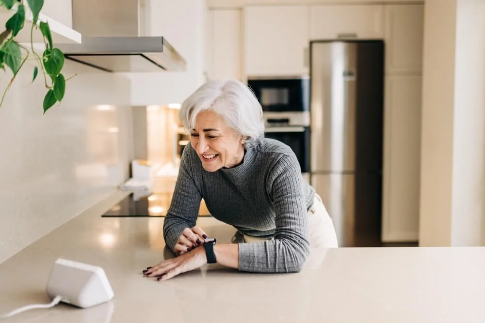 Woman leaning over kitchen counter looking at smart device.
