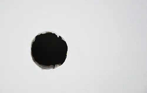 Hole in white wall from failed DIY picture hanging attempt.