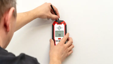 Man is using a stud finder to mark on an interior wall.