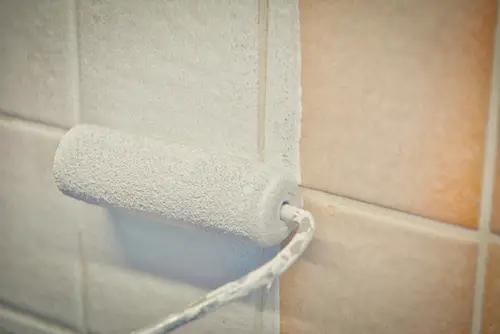 Close-up of painting bathroom tile with white paint
