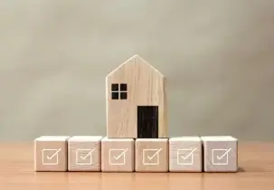 Wooden block house sitting on smaller blocks with check marks.