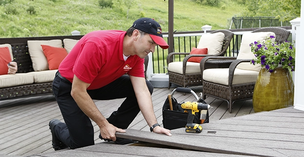 A Mr. Handyman professional setting a floorboard for deck repair.