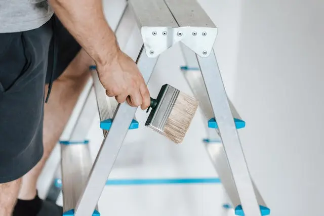 Close-up shot of a man holding a paint brush as he climbs a ladder.