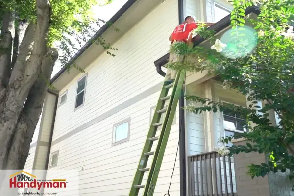 Mr. Handyman technician cleaning house gutters on a ladder during a professional home maintenance service