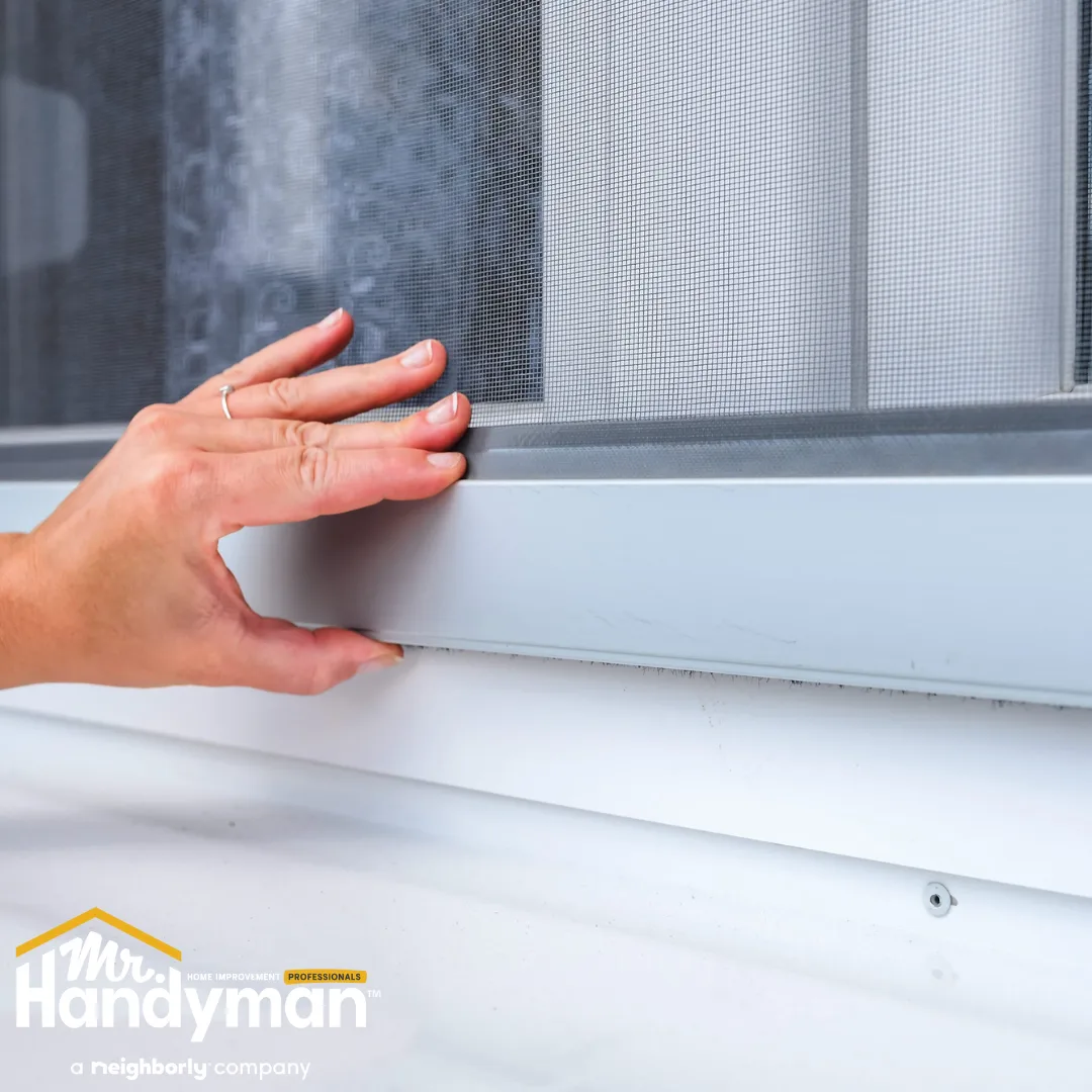A hand adjusting a window screen on a sliding window frame.