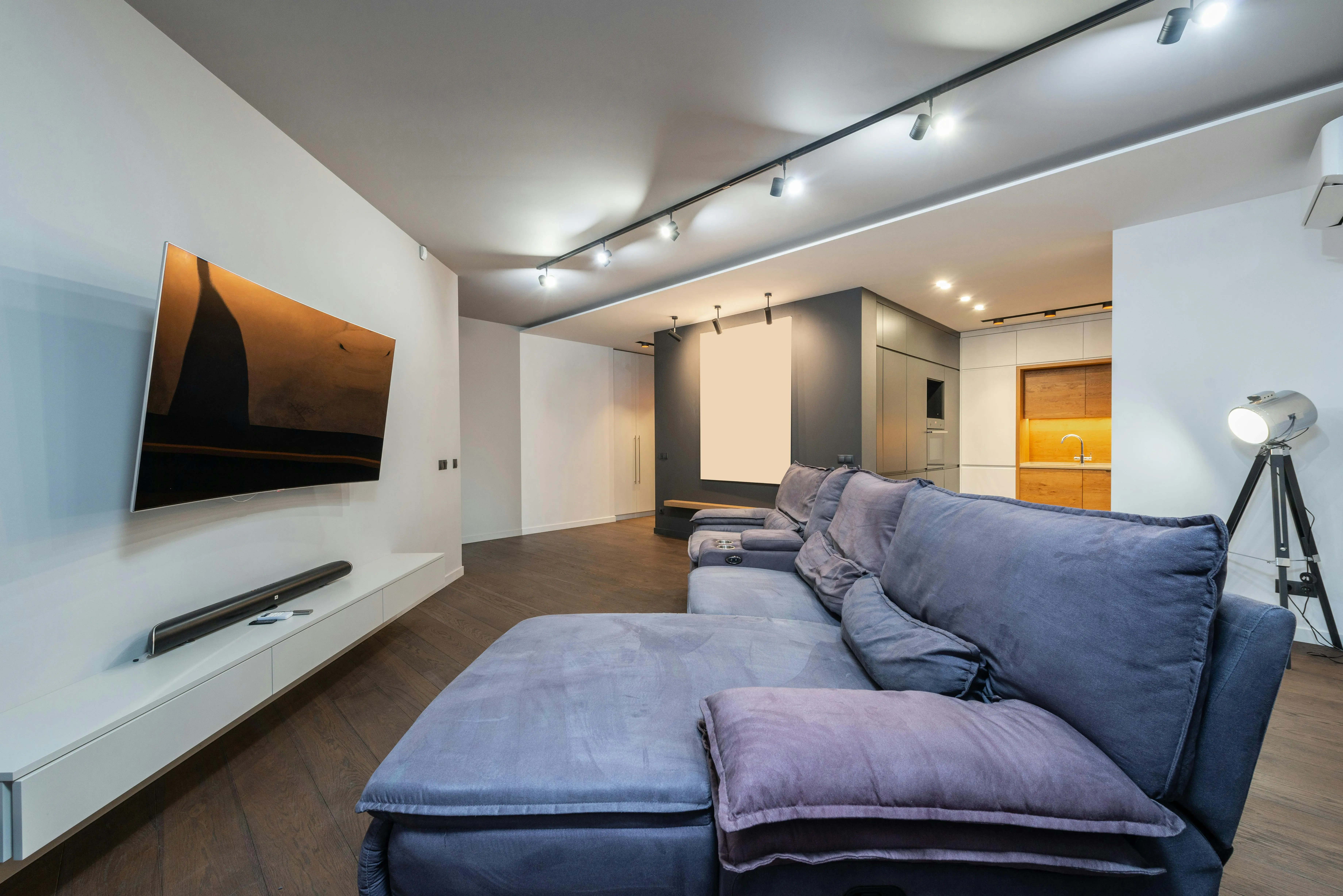 A grey couch in a brightly lit living room sits in front of a mounted TV with a sound bar underneath.