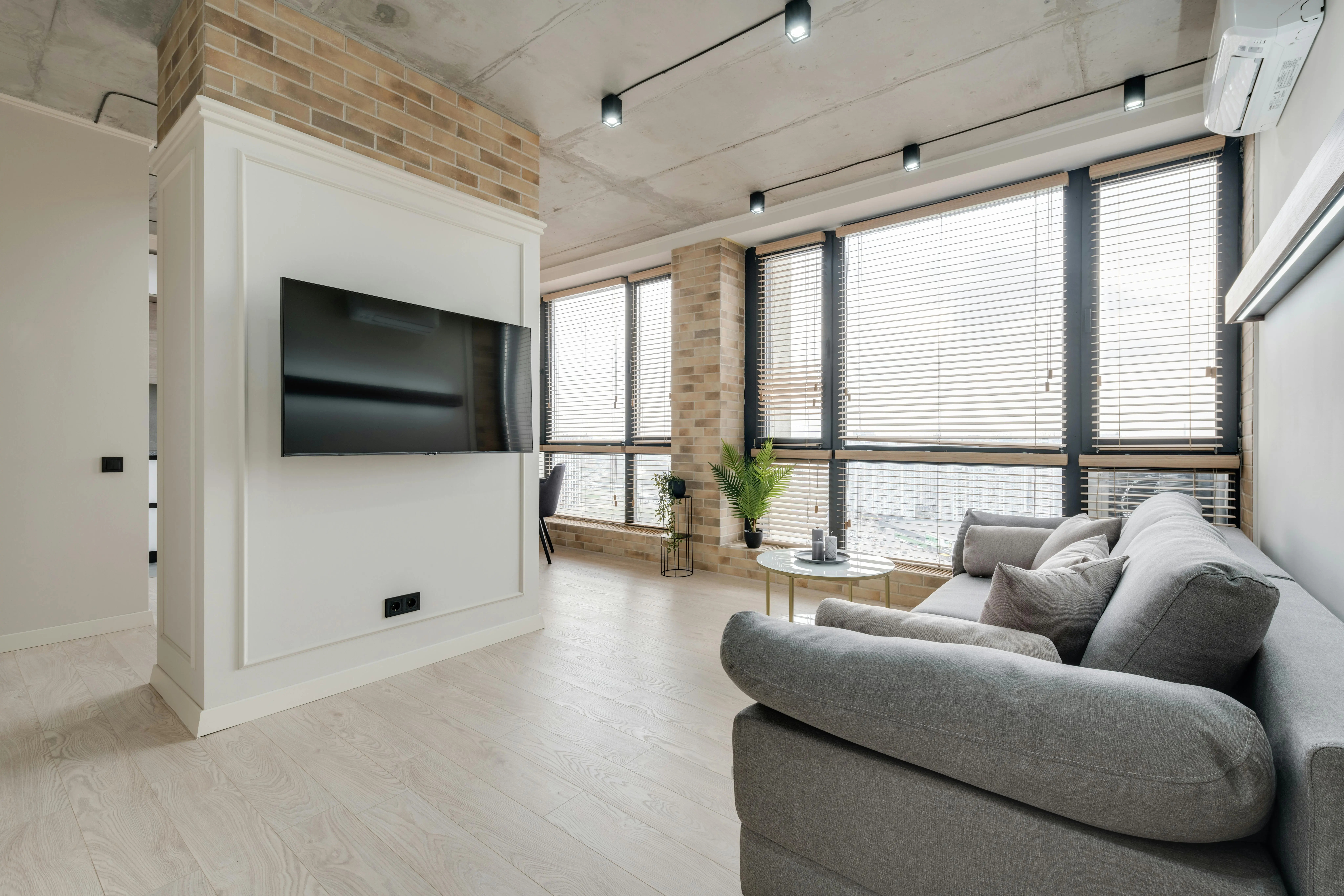 A grey couch sits in a room with floor-to-ceiling windows in front of a mounted TV.
