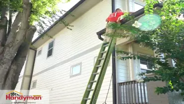 Mr. Handyman technician cleaning house gutters on a ladder during a professional home maintenance service