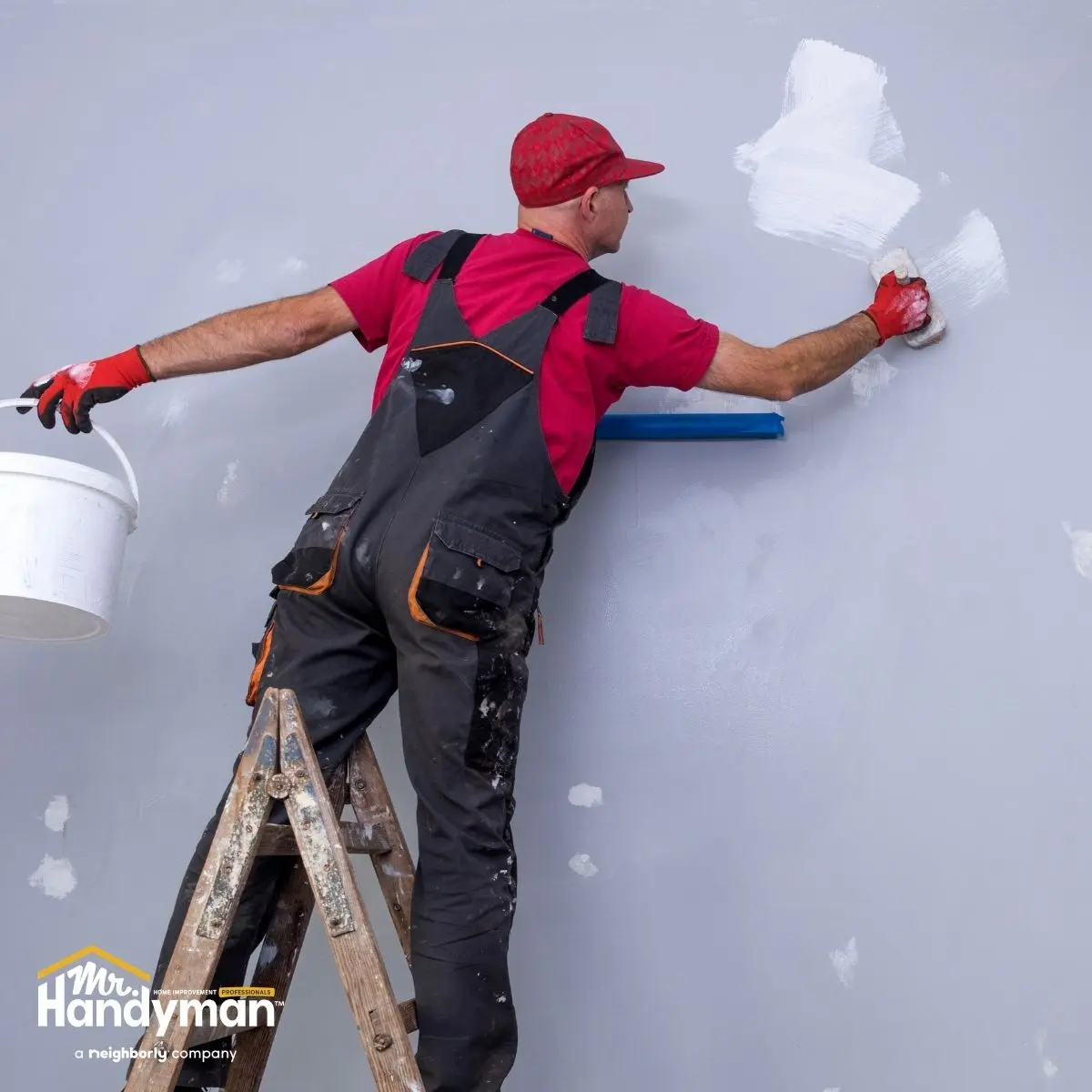 A worker in a red shirt and gloves is painting a wall.