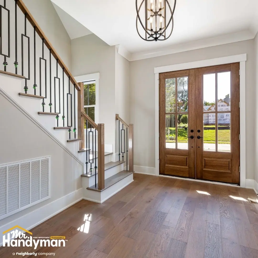 Bright entryway with wooden double doors, hardwood floors, and a staircase with metal railings.