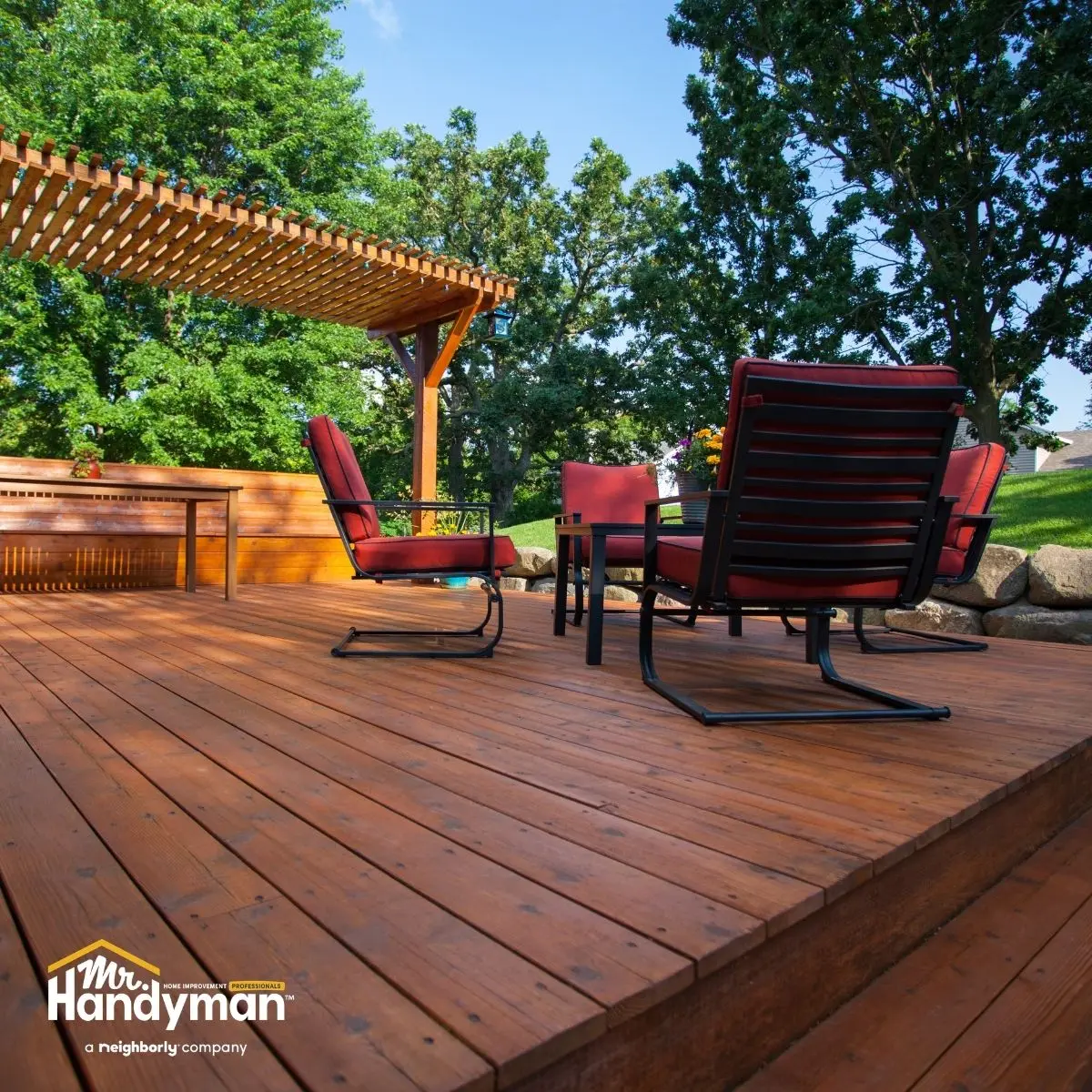 A wooden deck with red cushioned chairs and a table, under a pergola.