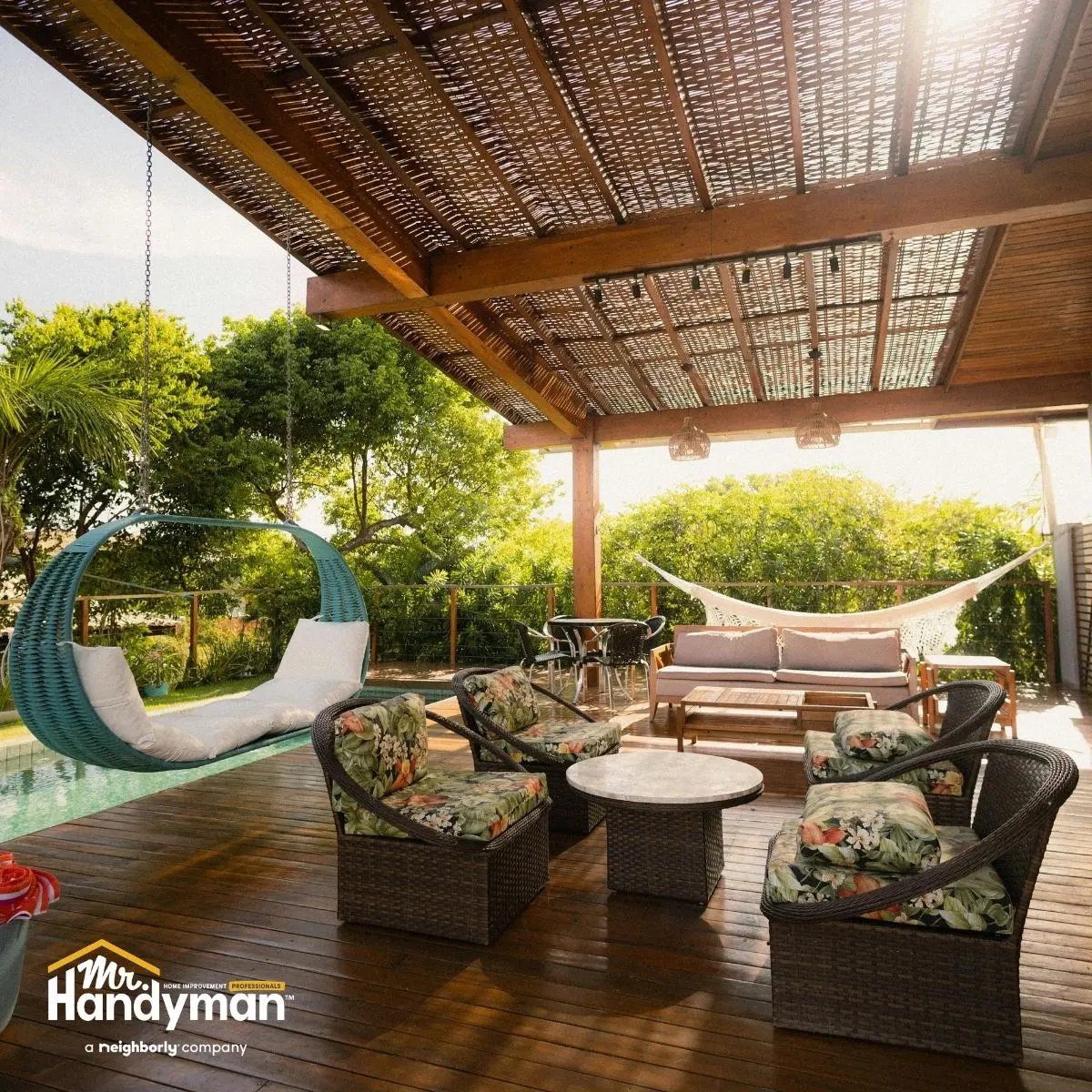 A covered outdoor patio with wicker seating, a hanging chair, a hammock, and a wooden floor, surrounded by greenery.