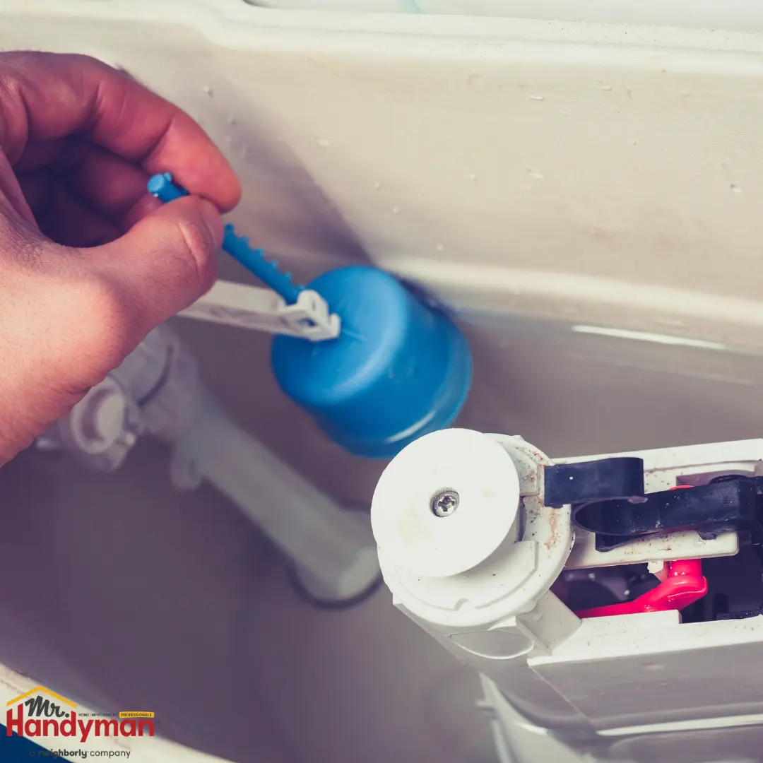 A hand adjusts a blue plastic float inside a white toilet tank.