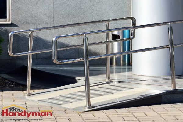 A low outdoor ramp with shiny stainless steel handrails leading up to a building entrance.