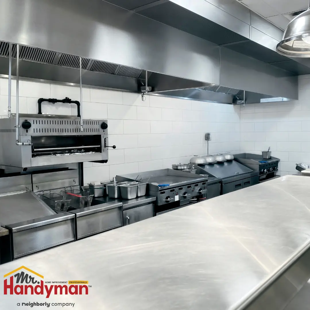 A modern commercial kitchen equipped with stainless steel countertops, industrial ovens, and a large wall-mounted ventilation hood.