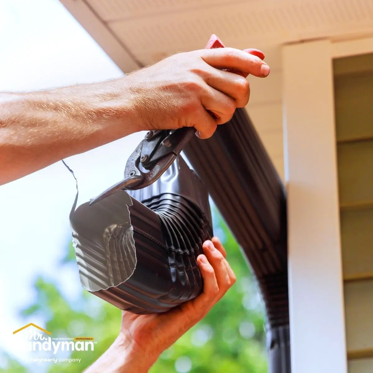 hands using tin snips to cut a dark metal to a house.