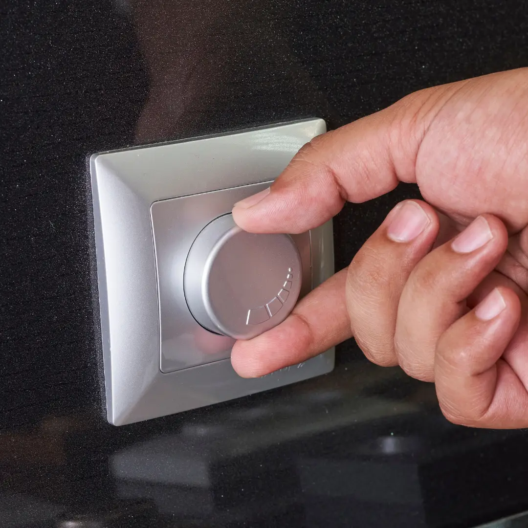 A hand adjusts a silver circular dial on a square wall-mounted control panel.